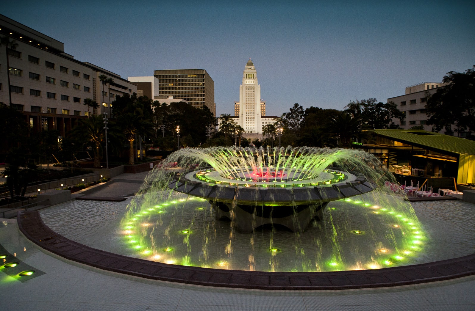 Image of a water fountain with yellow-green colors & tall buildings in view